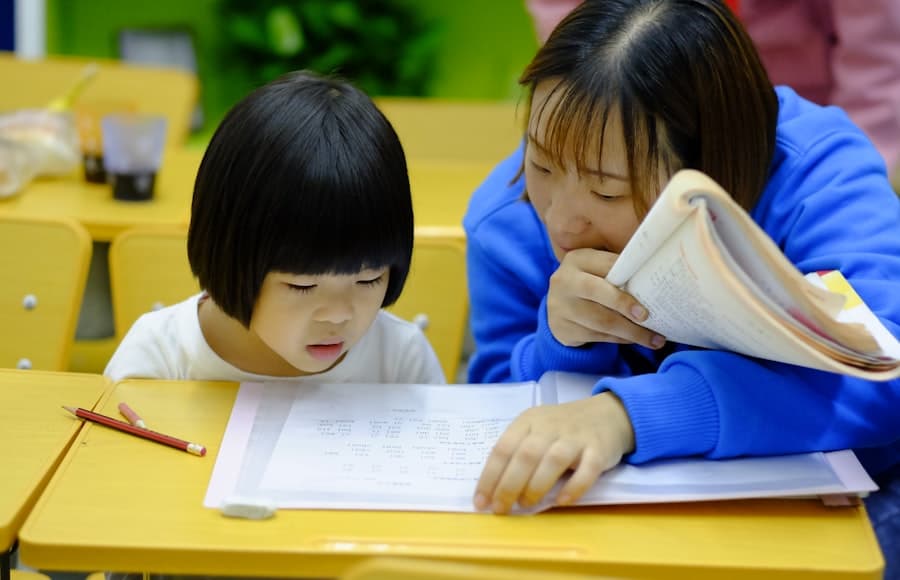 Two young children writing together at a classroom desk.